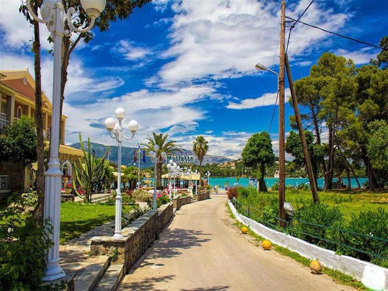Brede promenade in een zonnig groen park met palmbomen en een meer op de achtergrond.