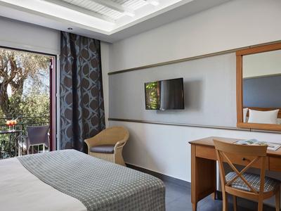 Modernes Hotelzimmer mit Bett, Schreibtisch, Stuhl und Balkon mit Blick ins Grüne.