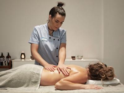 Eine Masseurin massiert den Rücken einer liegenden Frau in einem ruhigen Spa-Raum.