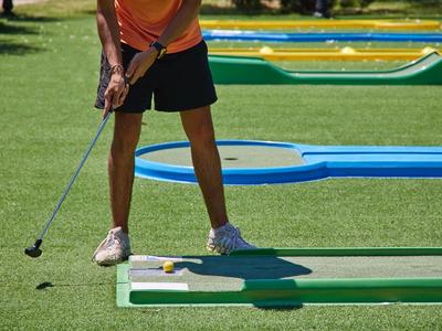 Person playing mini golf on a green course in bright sunlight.
