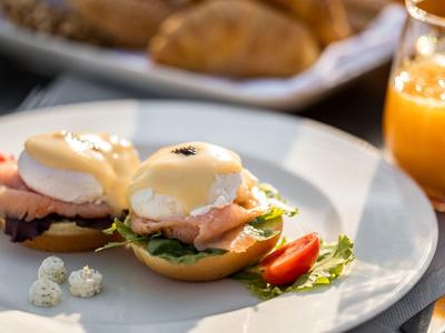 Zwei Eggs Benedict mit Lachs auf einem weißen Teller, dazu ein Glas Orangensaft.