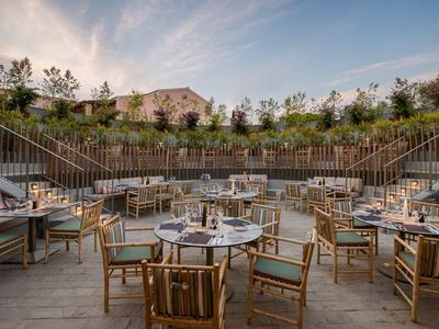 Außenrestaurant mit runden Tischen und Holzmöbeln in einer terrassierten Gartenanlage bei Sonnenuntergang