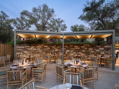 Outdoor restaurant with wooden chairs and tables, illuminated at dusk under trees.