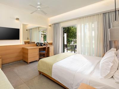 Helles Hotelzimmer mit Doppelbett, Schreibtisch, Deckenventilator und Glas-Schiebetür zum Balkon