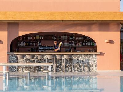 Open pool bar with bartender and stools next to a clear swimming pool at a hotel.