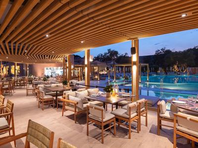 Elegantes Außenrestaurant mit Holzmöbeln und Blick auf beleuchteten Pool bei Dämmerung