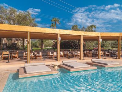 Modern outdoor pool with sun loungers and covered dining area under clear sky.