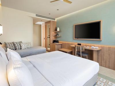 Modernes Hotelzimmer mit zwei großen Betten, TV, Schreibtisch und minimalistischer Einrichtung.