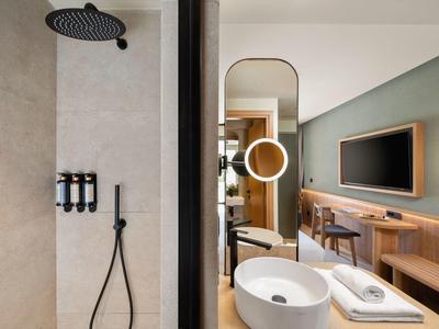 Modernes Badezimmer mit Dusche, Waschbecken, Spiegel und TV im Hotelzimmer