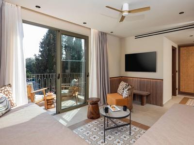 Helles Hotelzimmer mit zwei Betten, Balkon und Sitzbereich mit Tisch und Stühlen.