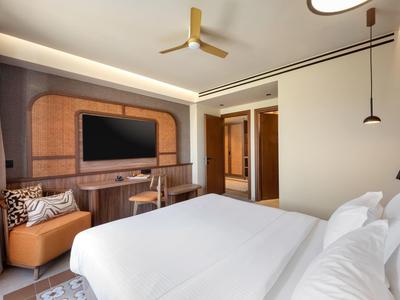 Modernes Hotelzimmer mit zwei Betten, TV an der Wand, Ledersessel und Schreibtisch.