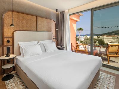 Modernes Hotelzimmer mit Doppelbett und Zugang zu Balkon mit Aussicht auf Garten und Meer.