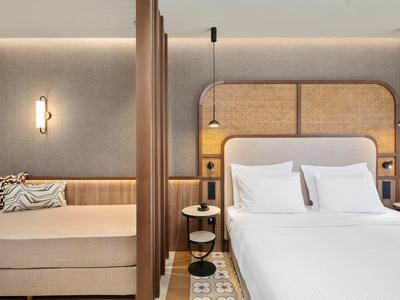 Modernes Hotelzimmer mit Doppelbett, Sofa und eleganter Beleuchtung in warmen Tönen.