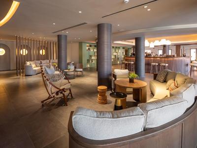 Moderner Hotel-Loungebereich mit bequemen Sofas, Sessel und Bartresen in warmem Licht.
