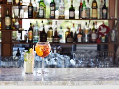 Zwei bunte Cocktails auf einer Marmorbar mit Spirituosenregal im Hintergrund.