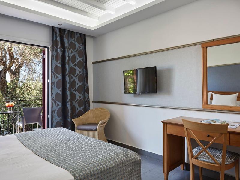 Modernes Hotelzimmer mit Bett, Schreibtisch, Stuhl und Balkon mit Blick ins Grüne.