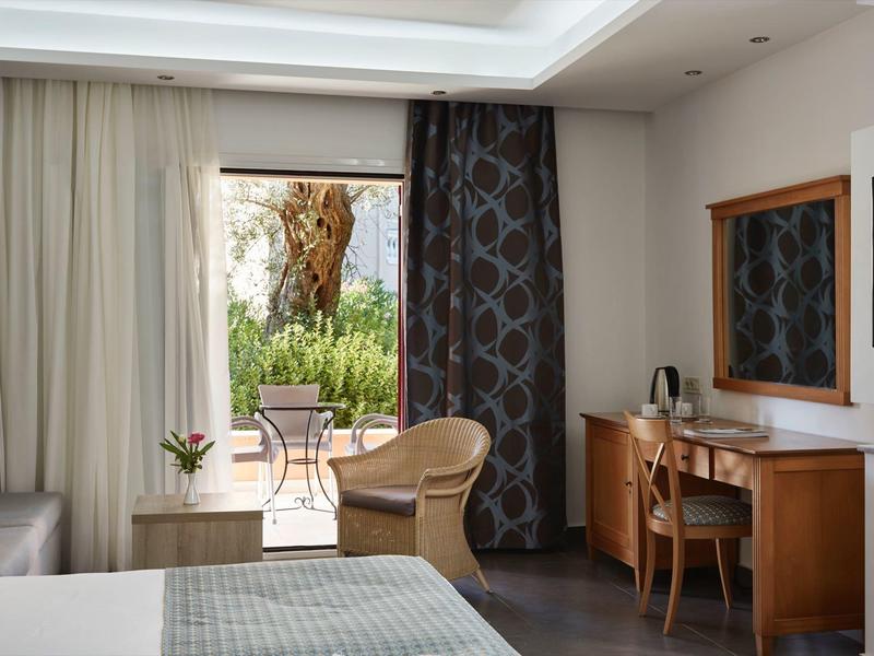 Hotelzimmer mit Bett, Schreibtisch, Sessel und Blick auf Terrasse und Garten