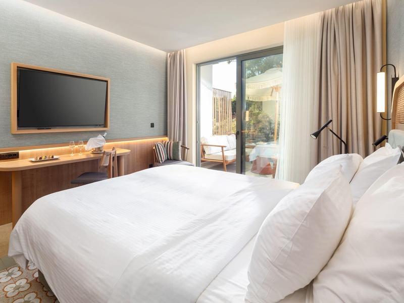 Modernes Hotelzimmer mit großem Bett, Schreibtisch und Glastür zur Terrasse.