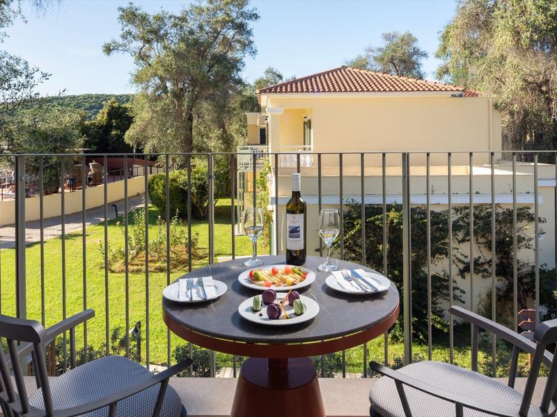 Balkon mit runden Tisch und zwei Stühlen, Blick auf grünen Garten und Wohnhaus.