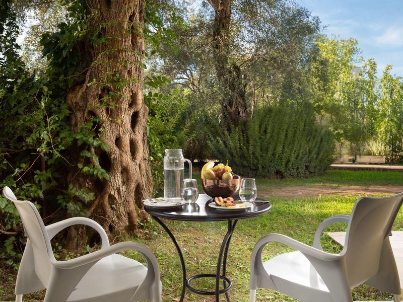 Kleiner runder Tisch mit Snacks und Getränken, umgeben von zwei weißen Stühlen im Garten.