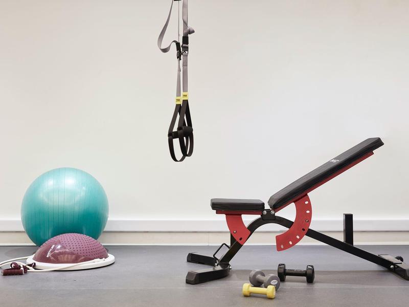 Fitnessraum mit Hantelbank, Gymnastikball, TRX-Schlingen und Kurzhanteln.