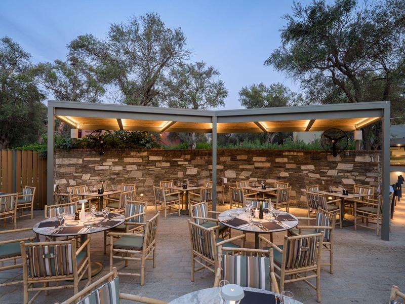 Modernes Outdoor-Restaurant mit Holzmöbeln, gedeckten Tischen und atmosphärischer Beleuchtung bei Dämmerung.