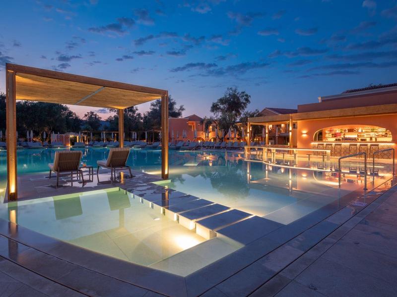 Abendaufnahme eines beleuchteten Hotelschwimmbeckens mit Lounge-Bereich und Sitzgelegenheiten.