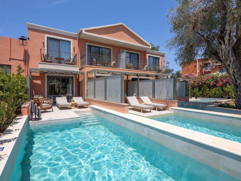 Modernes Ferienhaus mit Außenpool und Sonnenliegen, umgeben von Bäumen und klar blauem Himmel.