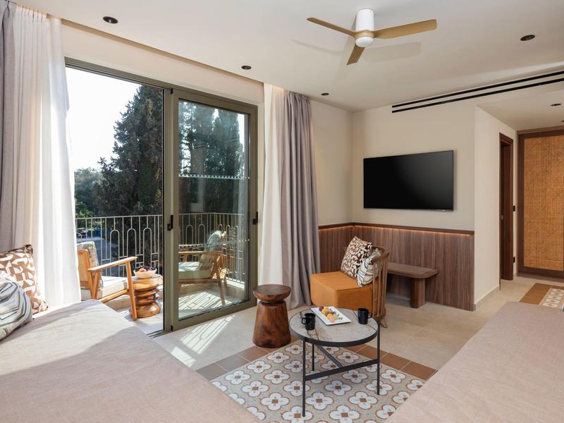 Helles Hotelzimmer mit zwei Betten, Balkon und Sitzbereich mit Tisch und Stühlen.