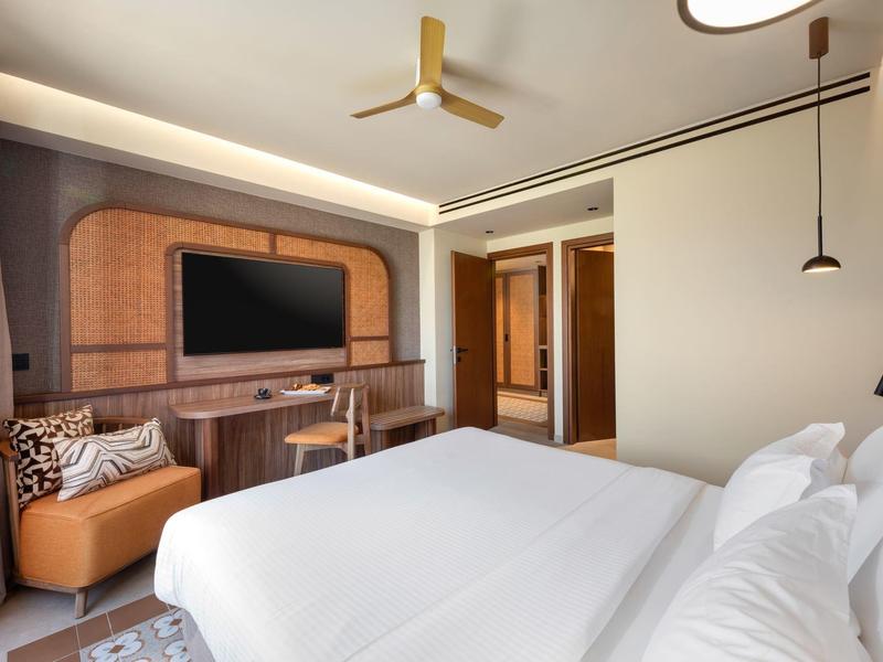 Modernes Hotelzimmer mit zwei Betten, TV an der Wand, Ledersessel und Schreibtisch.