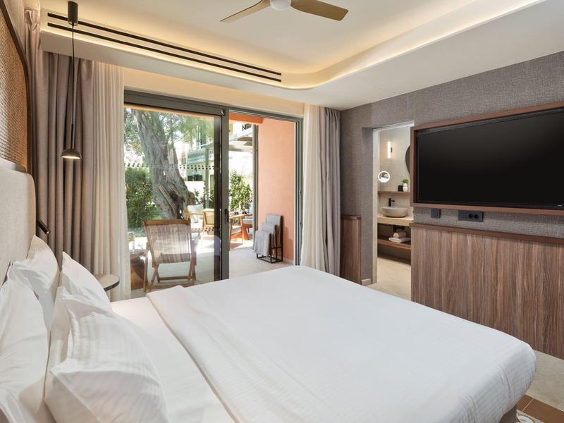 Modernes Hotelzimmer mit Doppelbett, TV und Zugang zu Terrasse mit Gartenblick.