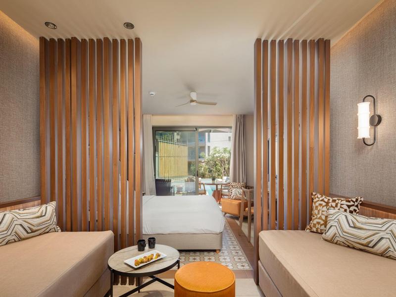 Modernes Hotelzimmer mit zwei Sofas, rundem Tisch und Doppelbett neben einer großen Fensterfront.