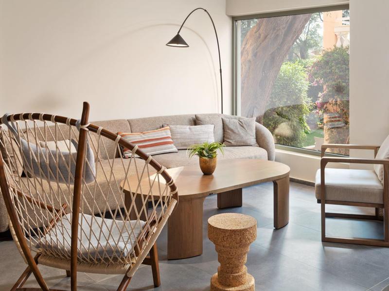 Hell eingerichtetes Wohnzimmer mit großen Fenstern, Sofa, Stühlen und einem runden Holztisch.