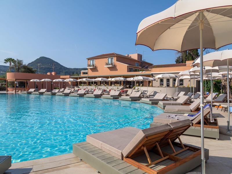 Großer Poolbereich mit Sonnenliegen und Sonnenschirmen in einem Hotel bei klarem Himmel.