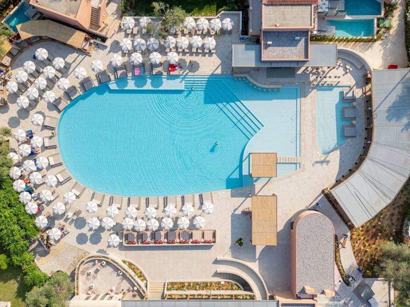 Vogelperspektive auf einen großen Hotelpool mit Liegestühlen und Sonnenschirmen außen herum.
