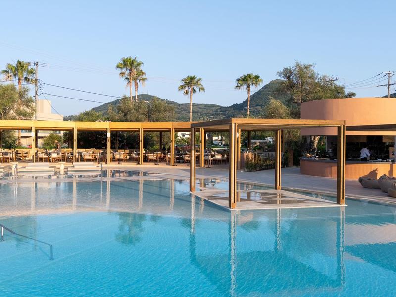 Ein großer Pool mit klarem Wasser, umgeben von einer überdachten Sitzbereich und Palmen im Hintergrund.