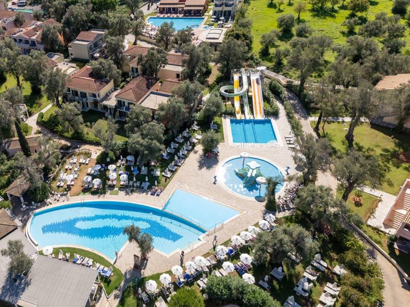 Luftaufnahme eines Hotelpools mit Wasserrutschen, umgeben von Bäumen und Gebäuden.