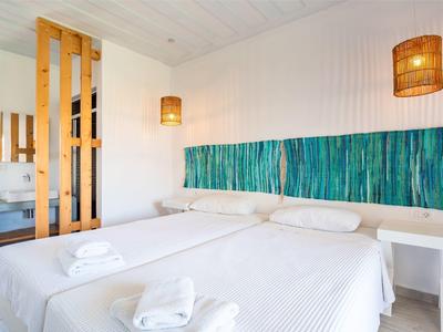 Helles Schlafzimmer mit zwei Einzelbetten, weißer Bettwäsche, blau-grünem Kopfteil und Holzlampen.