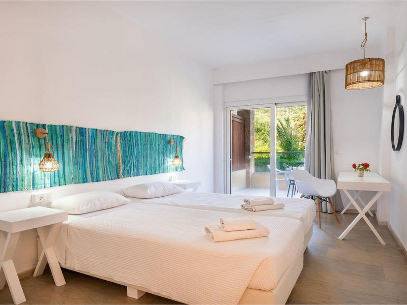 Bright hotel room with two single beds, white linens, turquoise headboard, and balcony access.