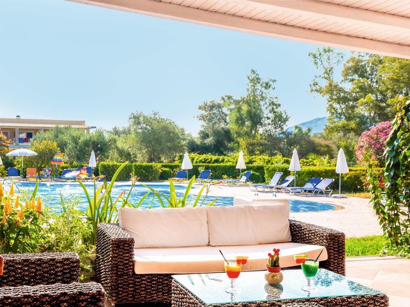 Outdoor seating area with wicker furniture overlooking a pool and garden with sun umbrellas.