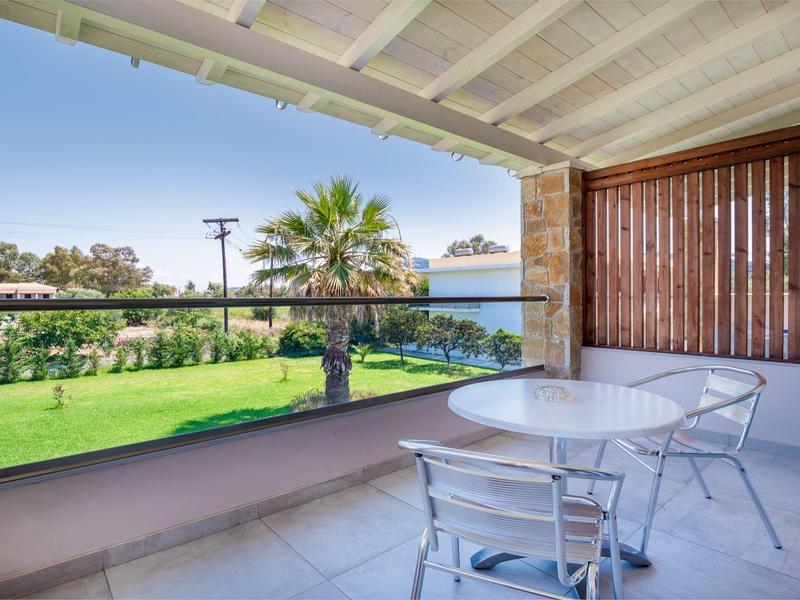 Balcony with white table and chairs overlooking green lawn and palm tree.