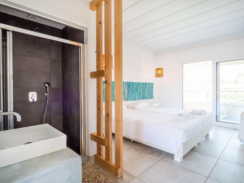Bright hotel room with white beds and a modern black-tiled shower area separated by wooden slats.