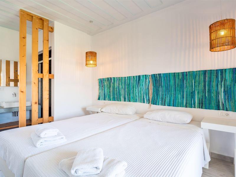 Minimalist hotel room with twin beds, white linens, wooden accents, and teal wall decor.