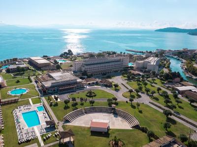 Vue aérienne d'un hôtel en bord de mer avec piscines et jardins verts par temps ensoleillé.