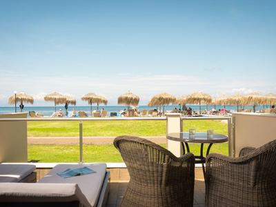 Vue depuis une terrasse avec des chaises donnant sur une plage avec des parasols en paille et une mer bleue.