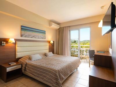 Chambre d'hôtel lumineuse avec lit double, TV, bureau et balcon avec vue sur le paysage.