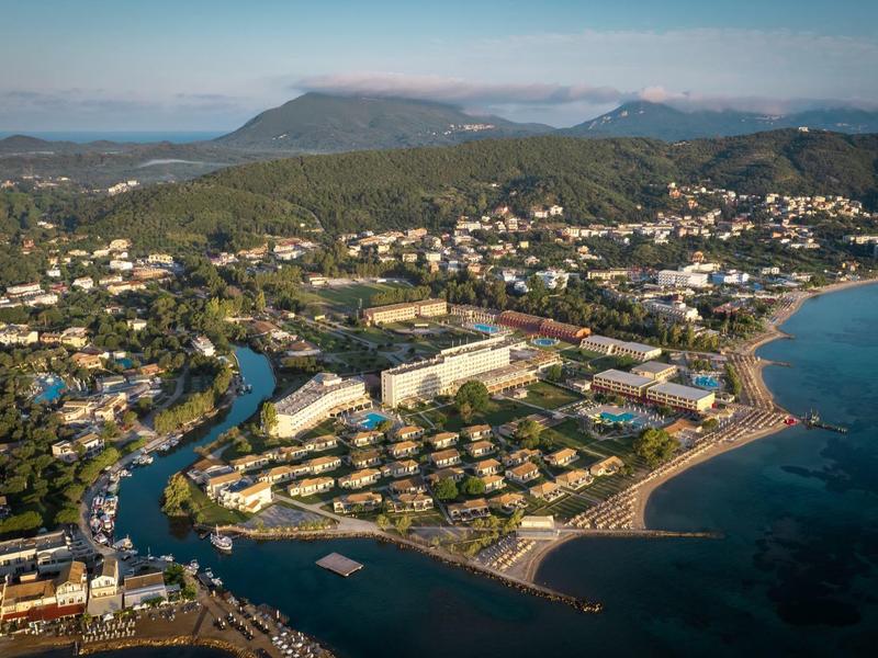 Vue aérienne d'une ville côtière avec plage, rivière et montagnes environnantes au coucher du soleil.