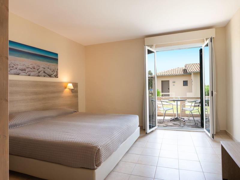 Une chambre d'hôtel simplement meublée avec un lit double et une porte ouverte sur le balcon.