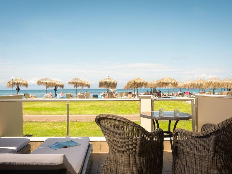 Vue depuis une terrasse avec des chaises donnant sur une plage avec des parasols en paille et une mer bleue.