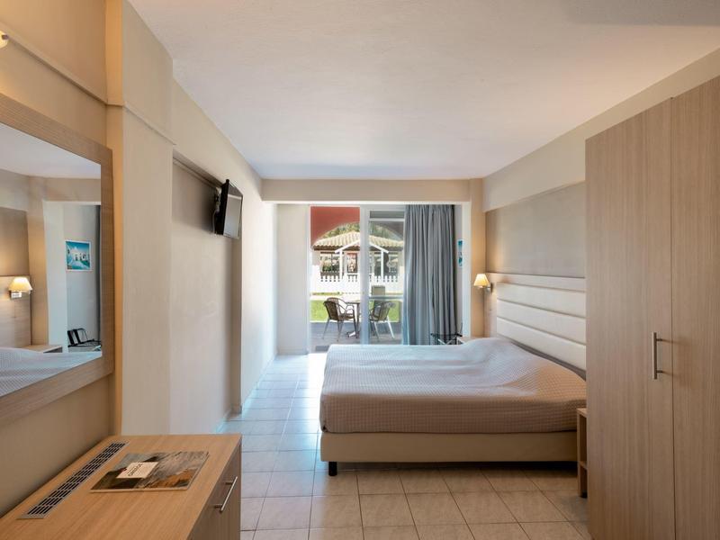 Chambre d'hôtel lumineuse avec lit double, armoire et vue sur la terrasse et le jardin.